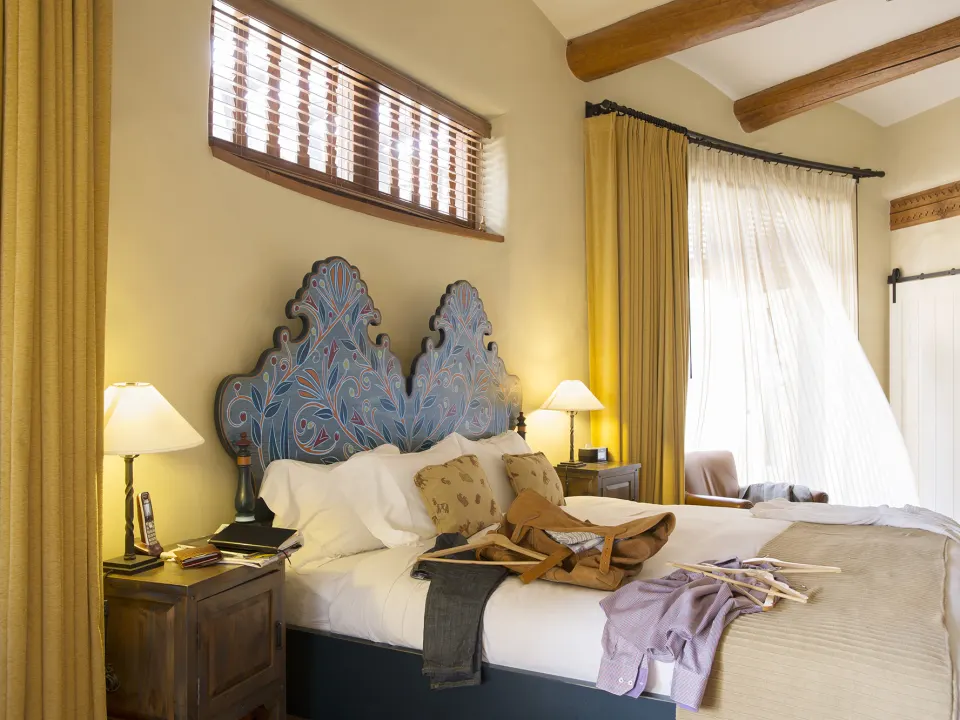 Chambre d'hôtel élégante avec un grand lit à tête sculptée, des rideaux dorés et une lampe de chevet allumée